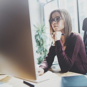 Attractive young businesswoman using desktop computer at modern working place at office.Blurred background.Horizontal.